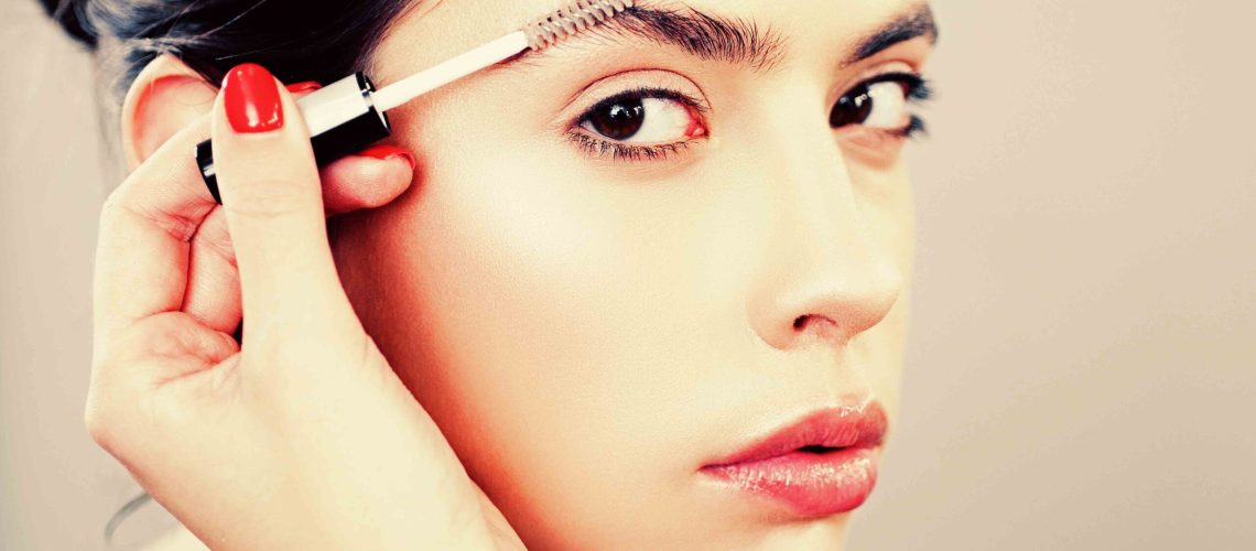 Care eyebrow. Makeup artist applying a brow gel on the eyebrows of a young beautiful woman with flawless nude natural makeup. Concept of professional make up doing